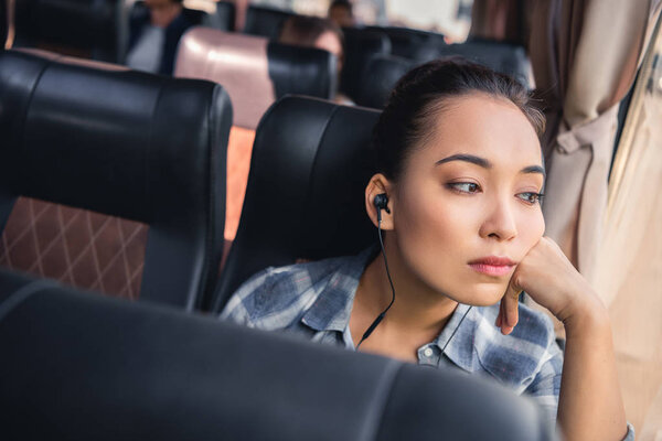 boring asian woman listening music in earphones during trip on travel bus 