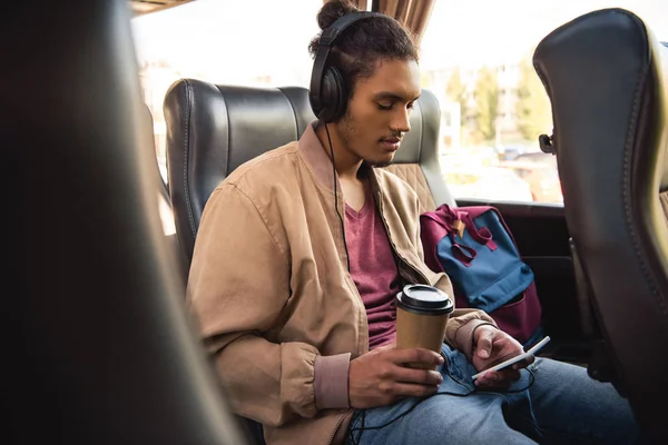 Multiracial Mandlige Turist Hovedtelefoner Sidder Med Papir Kaffekop Bruge Smartphone - Stock-foto