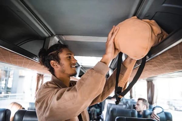 青年混血男子在旅游客车货架上放背包的侧视图 — 图库照片