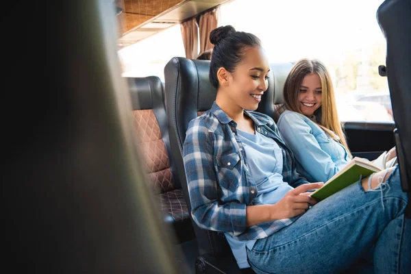 Roześmiany Wieloetnicznym Koleżanki Czytanie Książki Podczas Podróży Podróż Autobusem — Zdjęcie stockowe