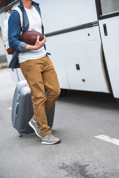 男子与背包和橄榄球球携带袋在车轮附近的旅游巴士在街道的裁剪图像 — 免费的图库照片