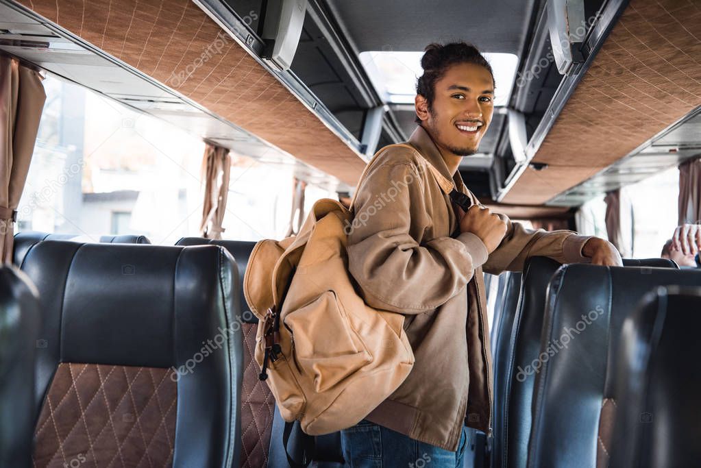 smiling multiracial male tourist with backpack looking at camera in travel bus