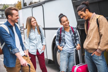 seyahat çantaları yakınındaki otobüs Street poz ile çok ırklı turistler gülüyor
