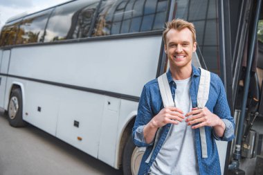 happy male tourist with backpack posing near travel bus at city street clipart