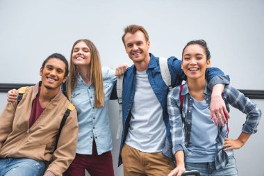 portrait of happy multicultural friends looking at camera near travel bus  clipart