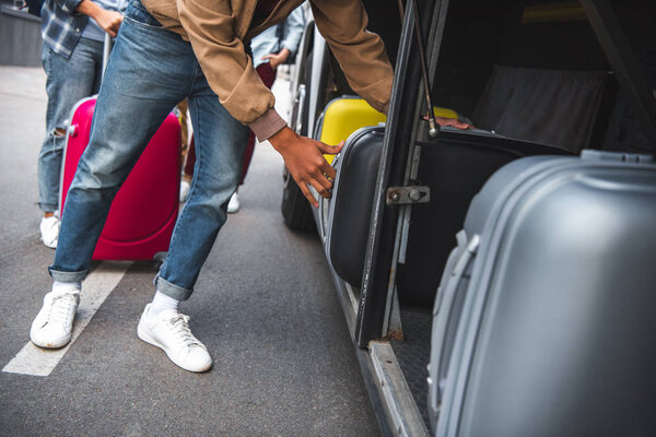 partial view of man putting wheeled bag into travel bus at city street 