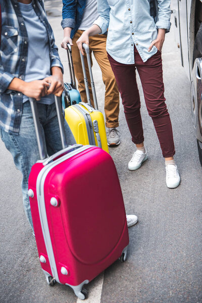 cropped image of tourists with wheeled bags standing near travel bus at urban street 