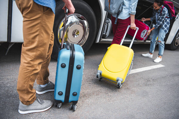 woman putting wheeled bag into travel bus while her friends walking near at urban street 