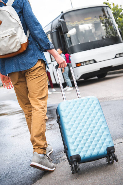cropped image of man with backpack carrying wheeled bag near travel bus at street
