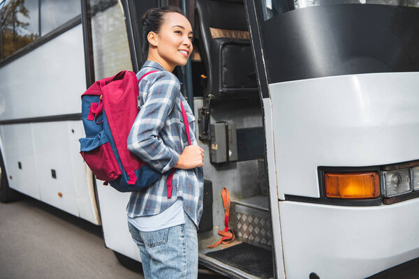 asian young woman with rucksack walking into travel bus at street