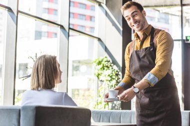 geniş gülümseyen genç garson servis kadın müşteri kafede kahve fincan