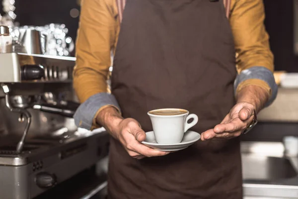 新鮮なコーヒーのカップを保持しているエプロンのバリスタのショットをトリミング — ストック写真