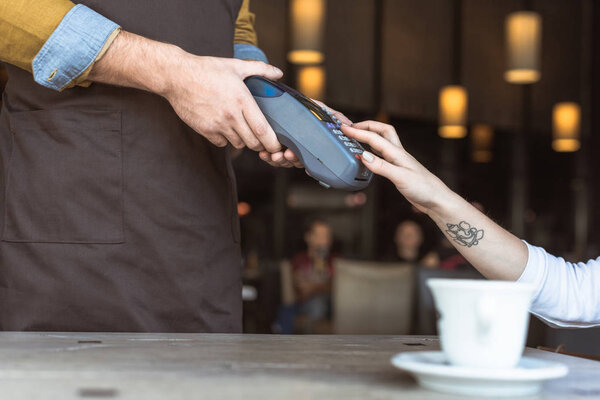 cropped shot of waiter holding payment terminal while client entering pin in cafe
