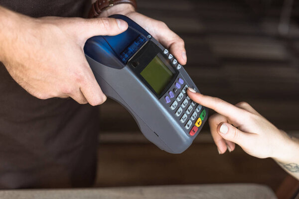 cropped shot of waiter holding payment terminal while customer entering pin in cafe