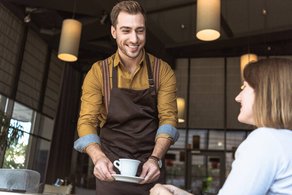 счастливый молодой официант, подающий чашку кофе клиентке в кафе
