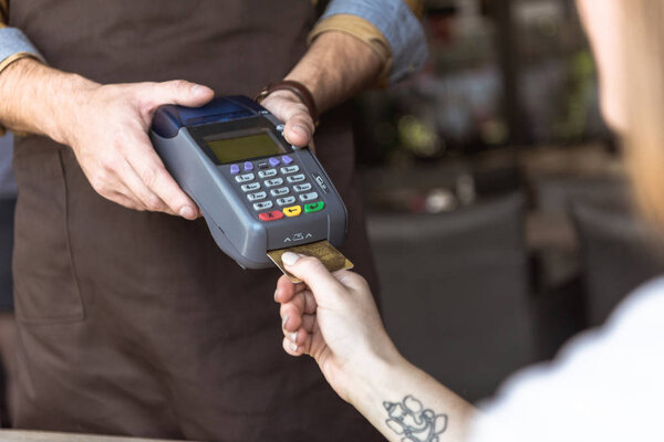 cropped shot of waiter holding payment terminal while customer inserting credit card