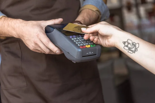 お支払いをお客様がカフェでクレジット カードと非接触式購入しながらターミナル保持ウェイターのショットをトリミング — ストック写真
