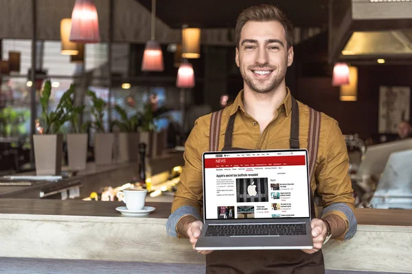 Przystojny Młody Kelner Trzymając Laptop Internetowej Bbc Ekranie Kawiarni — Zdjęcie stockowe