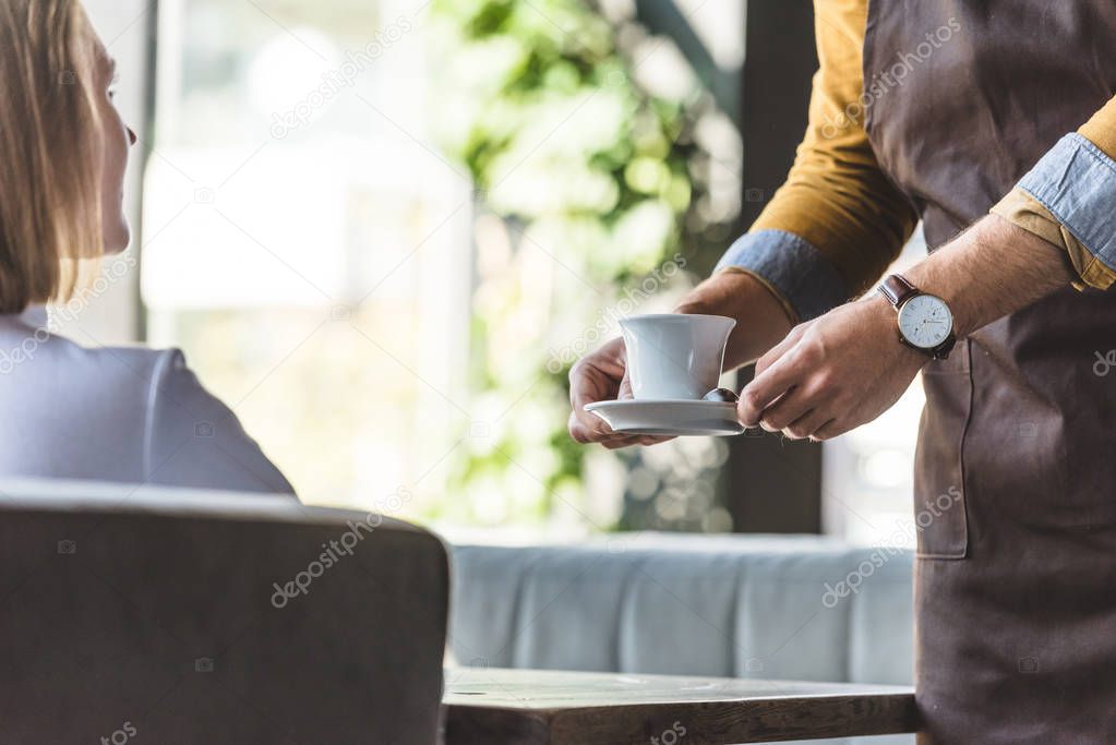 cropped shot of waiter serving cup of coffee for female client at cafe