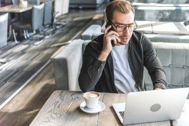 Laptop ile çalışma ve kafede telefonla konuşurken çekici genç serbest meslek