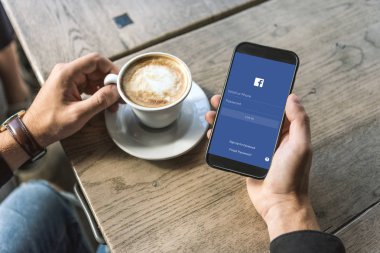 adam bardak fincan cappuccino ile facebook app üstünde perde smartphone kullanarak kırpılmış