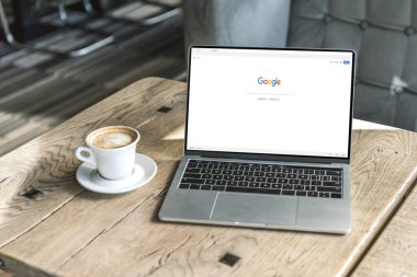 fincan kapuçino ve google web sitesinde kafede rustik ahşap masa üstünde perde ile dizüstü bilgisayar