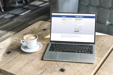 fincan kahve ve facebook Web sitesinde kafede ahşap masa üstünde perde ile dizüstü bilgisayar