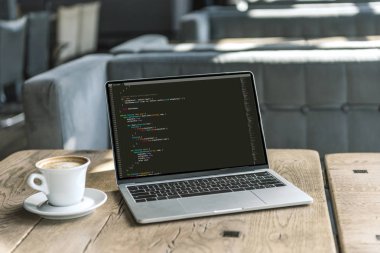 fincan kahve ve rustik ahşap masa kafede ekranda program kodu içeren dizüstü