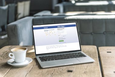 fincan kahve ve facebook Web sitesinde kafede rustik ahşap masa üstünde perde ile dizüstü bilgisayar