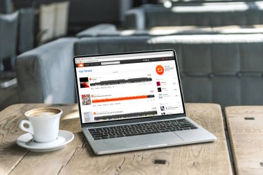 fincan kahve ve soundcloud Web sitesinde kafede rustik ahşap masa üstünde perde ile dizüstü bilgisayar