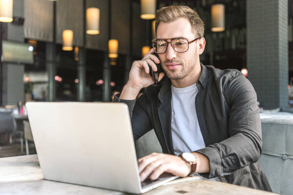 successful young freelancer working with laptop and talking by phone in cafe