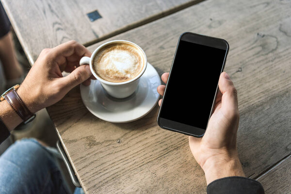 обрезанный снимок человека с чашкой капучино с помощью смартфона с пустым экраном
