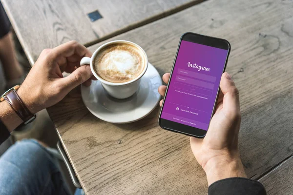 在屏幕上使用带有 Instagram 应用程序的智能手机的一杯咖啡的男子短款拍摄 — 图库照片