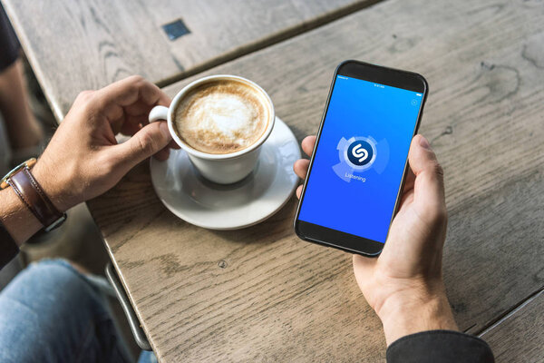 cropped shot of man with cup of cappuccino using smartphone with shazam app on screen