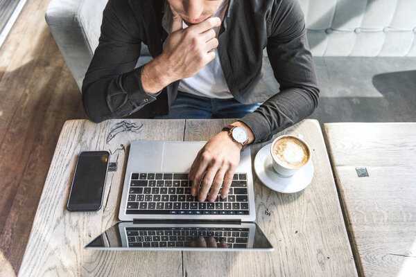 high angle view of thoughtful freelancer working with laptop in cafe