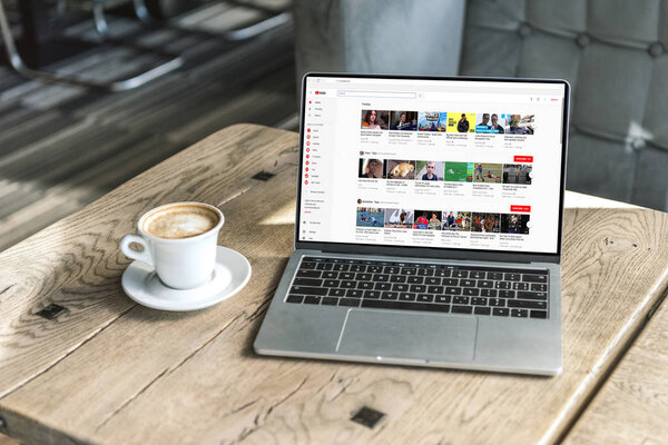 cup of coffee and laptop with youtube website on screen on wooden table at cafe