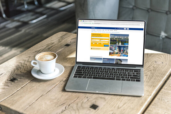 cup of coffee and laptop with booking website on screen on rustic wooden table at cafe