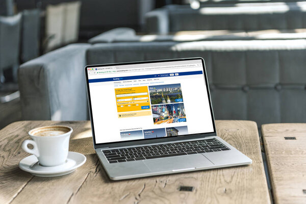 чашка кофе и ноутбук с бронированием сайта на экране на деревенском деревянном столе в кафе
