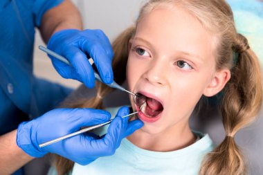 cropped shot of dentist with tools examining teeth of little child clipart