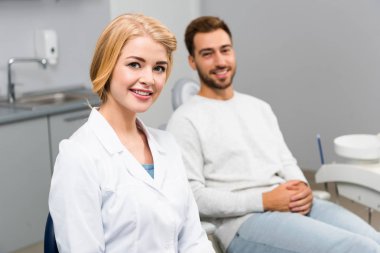 kadın diş hekimi ve diş hekimi office kamerada bakarak yakışıklı genç istemci gülümseyen