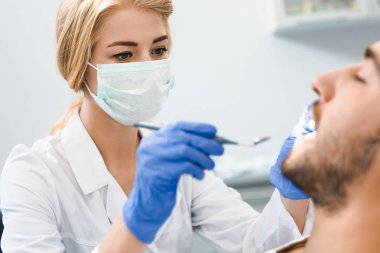 Genç kadın dişçi diş yakışıklı gülümseyen istemcisinin incelenmesi