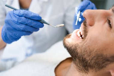 cropped shot of dentist examining teeth of handsome smiling client clipart