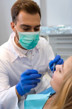 maskeli kadın müşteri diş inceleyerek genç diş hekimi