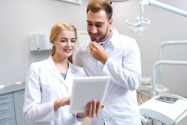 young male and female dentists working with tablet together clipart