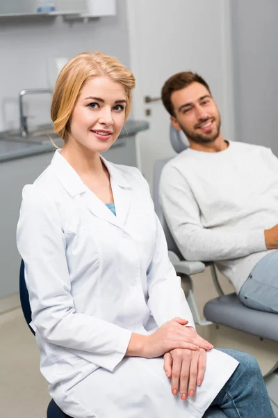 Felice Dentista Femminile Bel Giovane Cliente Guardando Fotocamera Nello Studio — Foto stock gratuita