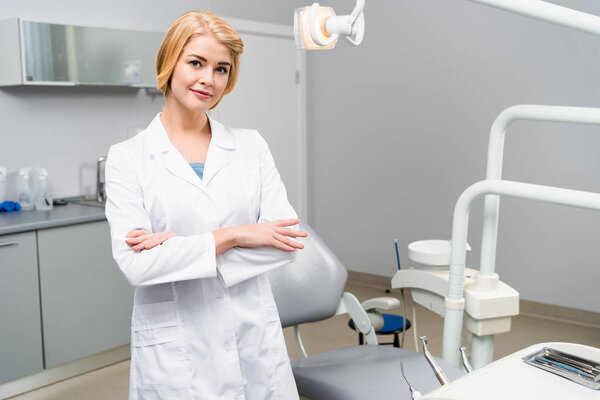attractive young dentist with crossed arms looking at camera in office