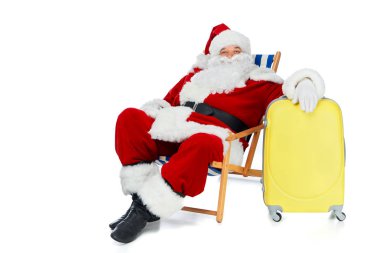 sakallı Noel Baba plaj sandalye üzerinde beyaz izole sarı seyahat çantası ile rahatlatıcı