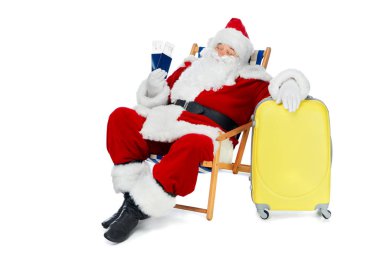 Noel Baba beyaz izole Bagaj ile plaj sandalyede otururken Noel tatil için tutan iki pasaport ve uçak bileti 