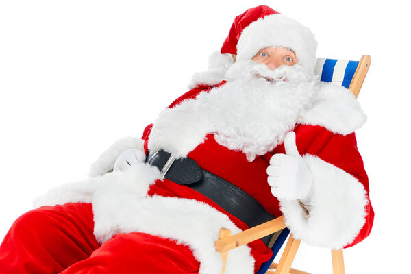 bearded santa claus showing thumb up and sitting in beach chair isolated on white