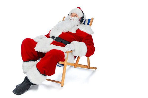 santa claus listening music with headphones while resting on beach chair on white